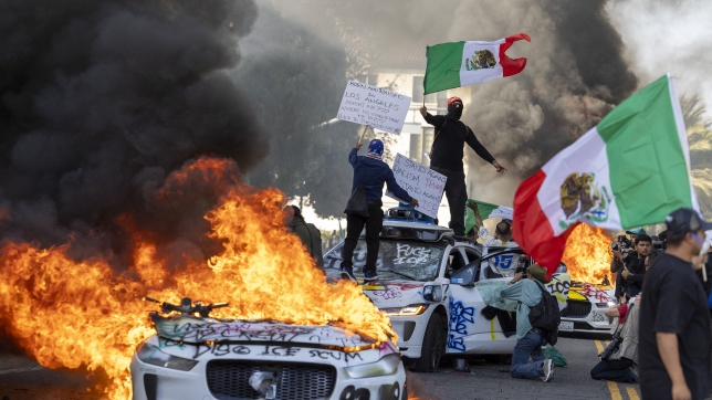 Des manifestants brandissent des drapeaux depuis le toit d’une voiture détruite, à côté de véhicules Waymo en feu, tandis que les protestataires s’affrontent avec les forces de l’ordre dans les rues autour du bâtiment fédéral lors d’une manifestation à la suite d’opérations fédérales sur l’immigration à Los Angeles, en Californie, le 8 juin 2025. Les manifestants ont incendié des voitures et se sont heurtés aux forces de sécurité alors que la police tenait les protestataires à distance des troupes de la Garde nationale envoyées dans les rues de la deuxième plus grande ville des États-Unis par le président Donald Trump. (Photo par RINGO CHIU / AFP)