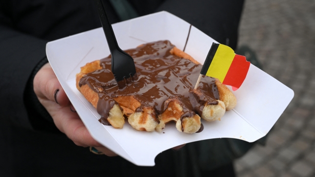 A tourist holds a Belgian waffle in the historical district in Bruges on December 30, 2024. (Photo by Nicolas TUCAT / AFP)
