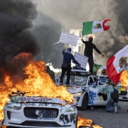 Des manifestants brandissent des drapeaux depuis le toit d’une voiture détruite, à côté de véhicules Waymo en feu, tandis que les protestataires s’affrontent avec les forces de l’ordre dans les rues autour du bâtiment fédéral lors d’une manifestation à la suite d’opérations fédérales sur l’immigration à Los Angeles, en Californie, le 8 juin 2025. Les manifestants ont incendié des voitures et se sont heurtés aux forces de sécurité alors que la police tenait les protestataires à distance des troupes de la Garde nationale envoyées dans les rues de la deuxième plus grande ville des États-Unis par le président Donald Trump. (Photo par RINGO CHIU / AFP)