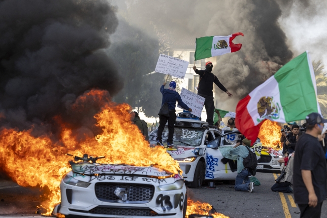 Demonstrators wave flags from atop a wrecked car, standing beside burning Waymo vehicles, as protesters clash with law enforcement in the streets surrounding the federal building during a protest following federal immigration operations in Los Angeles, California, on June 8, 2025. Demonstrators torched cars and scuffled with security forces in Los Angeles on June 8, as police kept protestors away from the National Guard troops President Donald Trump sent to the streets of the second biggest US city. (Photo by RINGO CHIU / AFP)