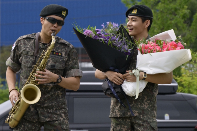 RM, membre du boys band K-pop BTS, joue du saxophone sous le regard de V, bouquets de fleurs à la main, dans un complexe sportif en plein air à Chuncheon, le 10 juin 2025, après leur libération de 18 mois de service militaire en Corée du Sud.