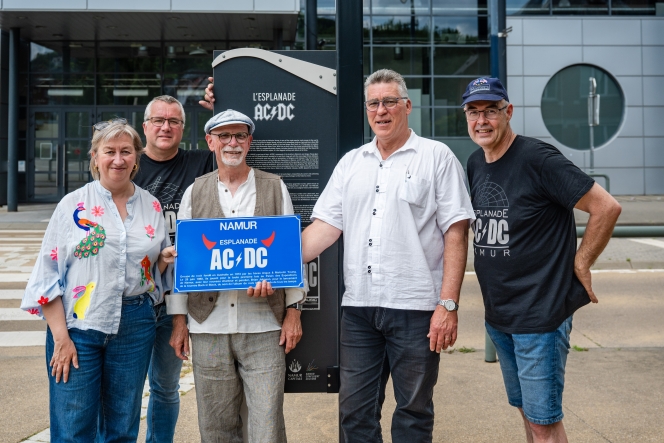 L’ancien bassiste du groupe de rock australien AC/DC Rob Bailey dévoile une chaise baptisée en son honneur, en posant avec les échevins Stéphanie Scailquin et Tanguy Auspert et Michel Remy et Mike Davister des « Amis de l’esplanade AC/DC ».